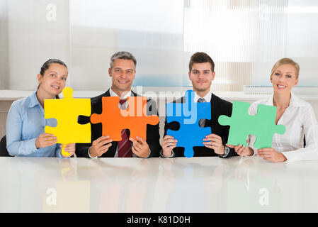 Team di imprenditori regge quattro multi-puzzle colorato a scrivania Foto Stock
