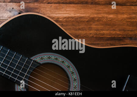 Nero chitarra acustica corpo closeup, su un invecchiato in legno marrone di sfondo della tabella, con un sacco di texture, che mostra la forma di chitarra Foto Stock