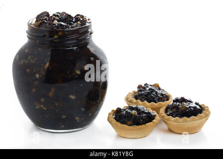 Vasetto pieno di mincemeat natalizio tradizionale fatto in casa con frutta mista con tre crostate di trincea a lato su uno sfondo bianco isolato Foto Stock