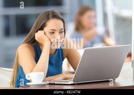 Annoiato donna guardare on line il contenuto in un laptop seduto in un bar terrazza Foto Stock