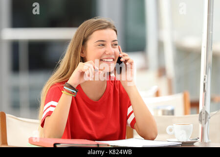 Candide studente ragazza ridere parlando al telefono ubicazione in un bar terrazza Foto Stock