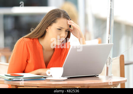 Preoccupati di imprenditore la lettura di cattive notizie sulla linea in un laptop seduto in un bar terrazza Foto Stock