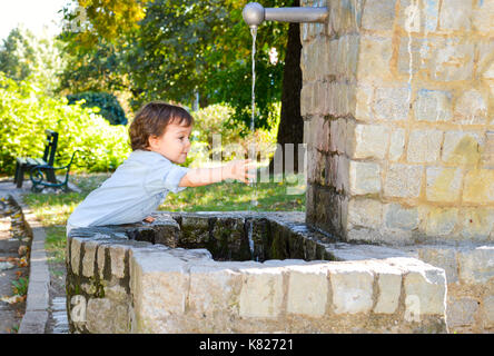 Felice ragazzo lavaggio delle mani in un parco Foto Stock