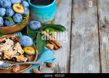 In casa tradizionale torta di prugne con cinamon e mandorle con caffè sul vecchio sfondo di legno Foto Stock