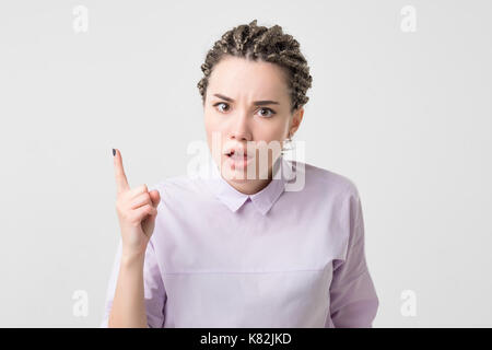 Ritratto di grave, accigliata, arrabbiato, scontroso giovane donna con trecce africane puntare il dito verso l'alto, scolding qualcuno Foto Stock