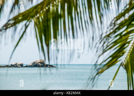 Guardando attraverso fronde di palme a rocce e mare al largo della costa di Ao Thang Nai Pan Noi su Koh Phangan / Ko Pha Ngan nel Golfo di Thailandia. Foto Stock