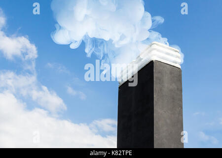 Il fumo aumenta da un camino in inverno giorno contro il cielo blu Foto Stock