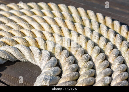 Cima nautica arrotolato a spirale sul molo in legno. Foto Stock