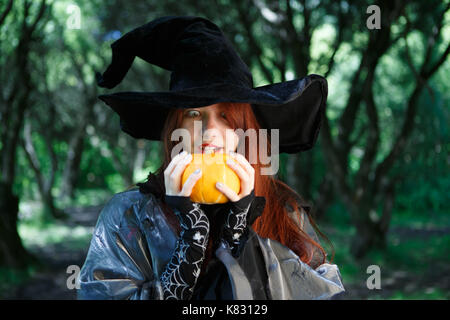 Fotografia di close-up di strega in black hat con zucca da affrontare nella foresta di mistico Foto Stock