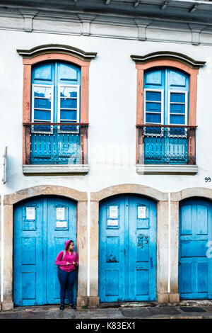 Una giovane donna in attesa per il trasporto nella parte anteriore di una casa coloniale di Ouro Preto, Minas Gerais, Brasile. Foto Stock