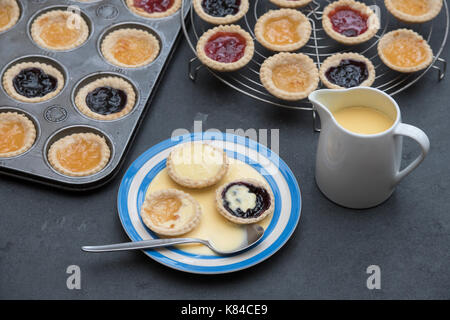 Cucinato in casa Crostate di confettura su una piastra con crema pasticcera accanto a un vassoio da forno e una circolare vintage filo rack Foto Stock