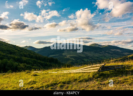 Rotture di recinzione di legno sul pendio erboso in montagne al tramonto. paesaggio con belle cloudscape oltre la cresta Foto Stock