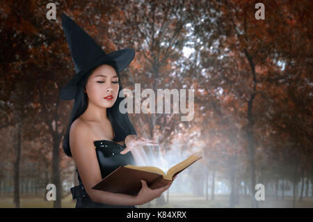 Giovane donna asiatica in costume delle streghe magia tenuta libro sulla foresta Foto Stock