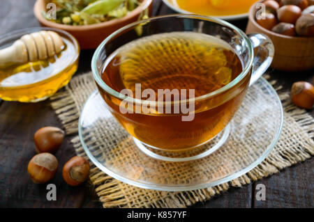 Un bicchiere di fresco e fragrante tè alle erbe con miele e nocciole su legno scuro dello sfondo. close-up. Foto Stock
