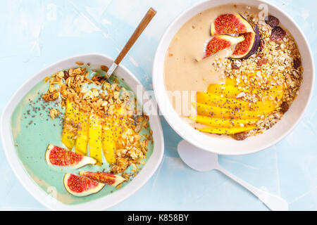 Spirulina e carruba smoothie bocce di granola, mango e fichi, blu sullo sfondo di calcestruzzo, vegan sana colazione concetto. Foto Stock