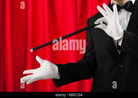 Close-up di mago in tuta che mostra trucco con la bacchetta magica Foto Stock