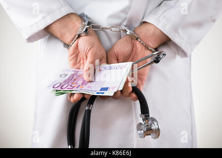 Close-up di un medico mani con banconote in euro e manette Foto Stock