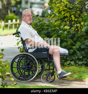 Uomo di mezza età con un'amputazione della gamba in una sedia a rotelle. Foto Stock