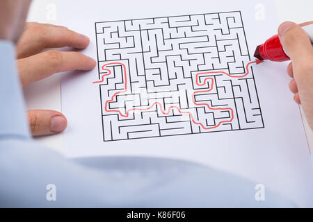 Close-up di persona con il rosso pennarello risolvendo puzzle maze Foto Stock