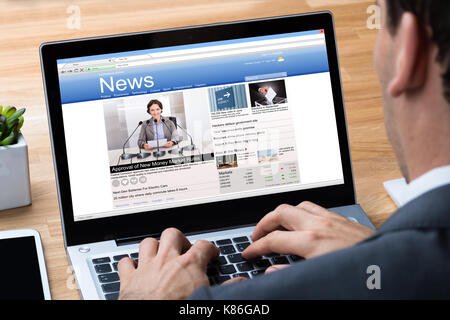 Immagine ritagliata di imprenditore per leggere le notizie sul portatile in ufficio Foto Stock