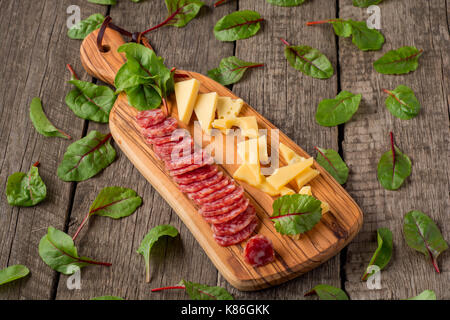 Formaggi e salumi su cucina di bordo su sfondo rustico. vista superiore con spazio di copia e le erbe aromatiche . Foto Stock