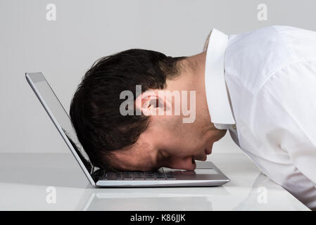 Vista laterale del sottolineato imprenditore appoggiata su laptop al banco contro uno sfondo bianco Foto Stock