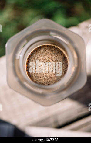 Fresca del mattino caffè aeropressed essendo prodotta all'esterno sul vecchio tavolo in legno sfondo Foto Stock