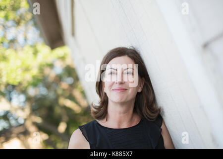 Una donna matura in una camicia senza maniche con lunghezza di spallamento brunette capelli mediante una parete bianca. Foto Stock