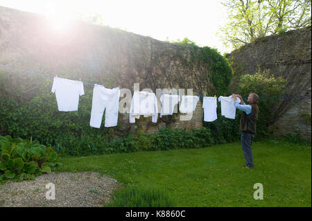 Uomo in piedi su un prato in un giardino, appendere biancheria sulla linea di lavaggio. Foto Stock