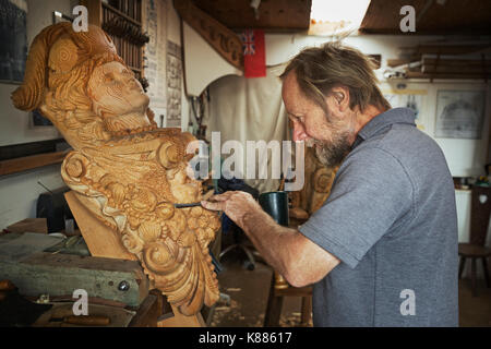 Un artigiano, un intagliatore di legno lavorando su una femmina di legno della nave polena trattenuto in una morsa sul banco di lavoro del suo workshop. Foto Stock