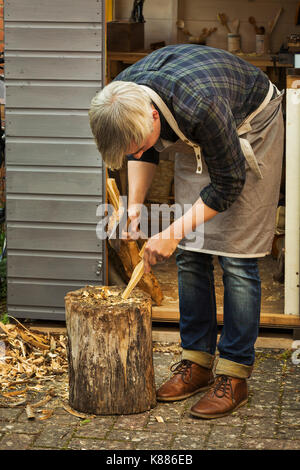 Artigiano intarsiatore la piegatura verso il basso e tenendo una mano ax, il taglio di un pezzo piccolo di legno su un blocco di suddivisione. Foto Stock