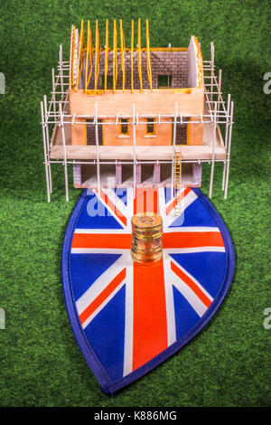 Nuovo modello di costruire casa su una Unione Jack, con nuovo sterling pound monete. Concetto raffiguranti qualsiasi aspetto dei costi per la proprietà del Regno Unito industria edilizia. Foto Stock