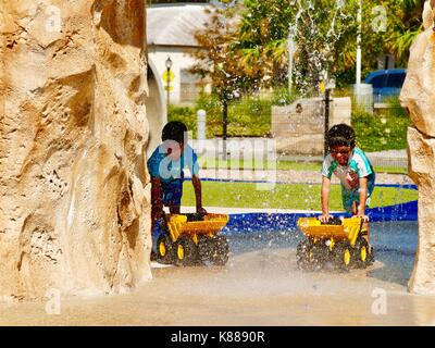 Due giovani ragazzi, che hanno un aspetto simile fratelli, giocando con il giocattolo, camion giallo sotto acqua a cascata allo splash park. Florida, Stati Uniti d'America. Foto Stock