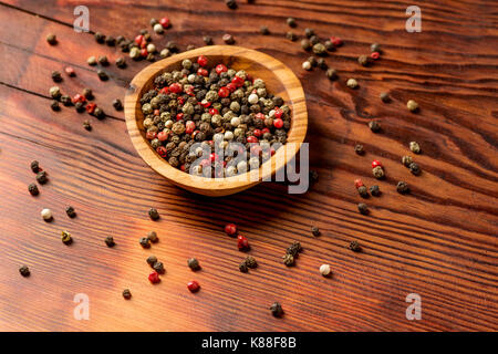 Grani di pepe in una ciotola di legno al buio su un sfondo di legno Foto Stock