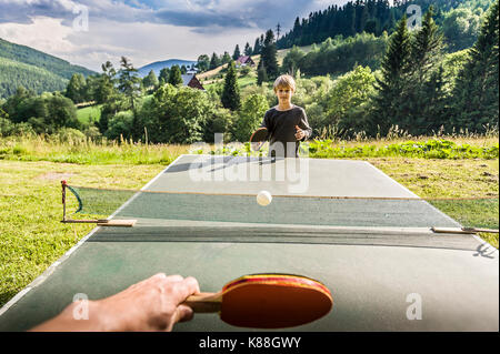 Scuola ragazzo giocando a ping-pong per esterno Foto Stock