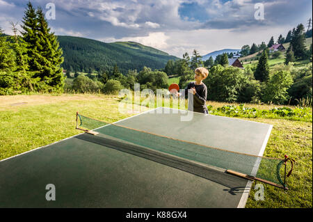 Scuola ragazzo giocando a ping-pong per esterno Foto Stock