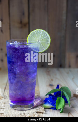 Butterfly pea succo con ghiaccio nella coppa trasparente servire su un tavolo di legno con fiore. Foto Stock