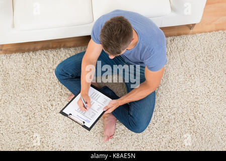 Angolo di alta vista del giovane uomo riempiendo il modulo del sondaggio nel soggiorno Foto Stock