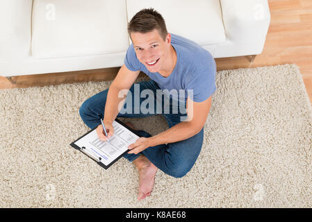 Angolo di alta vista del giovane uomo riempiendo il modulo del sondaggio nel soggiorno Foto Stock