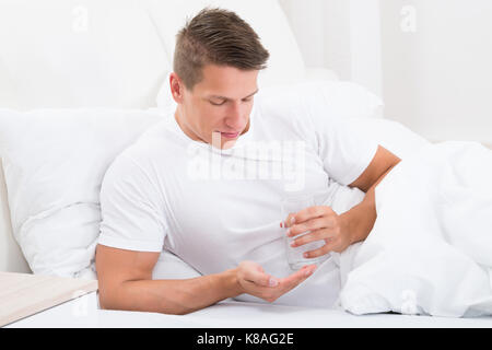 Giovane uomo nel letto di prendere la medicina con un bicchiere di acqua Foto Stock