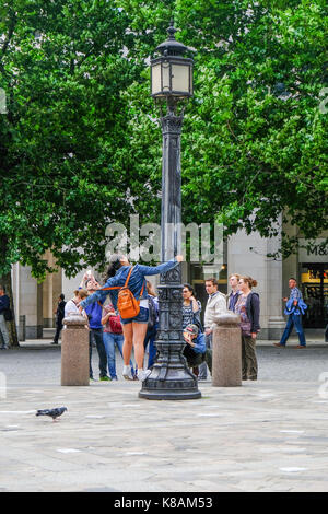 London, Regno Unito - 3 agosto 2017: Ragazza in posa su un lampione con un gruppo di turisti di scattare una foto. a giorno di colpo di scena di strada. Foto Stock