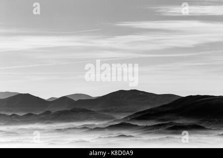 Una vista da sopra di una valle riempita da un mare di nebbia, con vari strati di emergenti colline e montagne Foto Stock