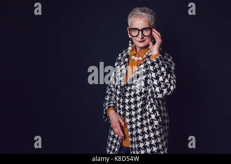 Eleganti e alla moda donna anziana in bicchieri su uno sfondo nero. Foto Stock