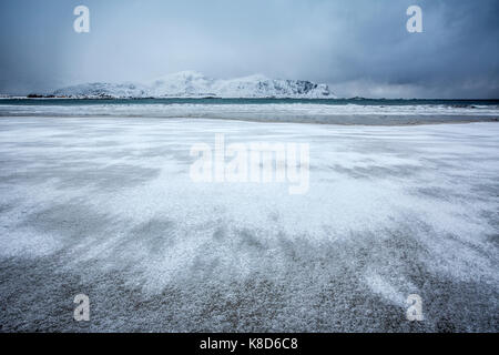 Onde del mare ghiacciato sulla spiaggia sullo sfondo le cime innevate ramberg isole Lofoten in Norvegia europa Foto Stock