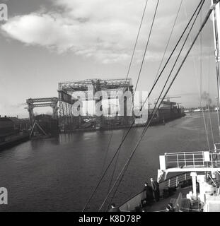 Anni '50, storico, una vista del portale Arrol, una grande struttura in acciaio al cantiere Harland e Wolff a Queen's Island, Belfast, Irlanda del Nord, Regno Unito. Commissionata dalla White Star Line e da Harland e Wolffe nel 1908, fu costruita per fungere da gru aeree per la costruzione di transatlantiche di classe olimpica, tra cui il famoso Titantic. Questo gigantesco portale è stato demolito negli anni '60, alcuni anni dopo questa foto dal fotografo inglese, J Allan Cash. Foto Stock