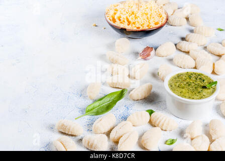 Materie non cotti in casa gnocchi di patate con farina, parmigiano grattugiato, basilico e pesto. su calcestruzzo fondo azzurro, spazio di copia Foto Stock