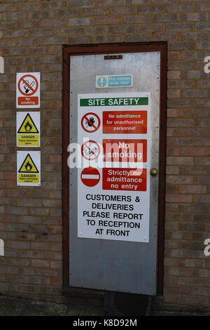 Un sicuro porta antincendio su un gruppo industriale con il sito avvertenze di sicurezza e le informazioni di poster Foto Stock