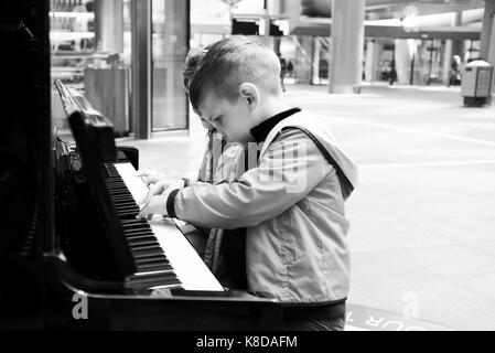 Little Boy giocando sul vecchio nero pianoforte all'aperto Foto Stock