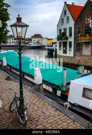 bicicletta con lampione su un sentiero acciottolato vicino alla chiatta ormeggiata sul fiume a Dordrecht, Paesi Bassi Foto Stock