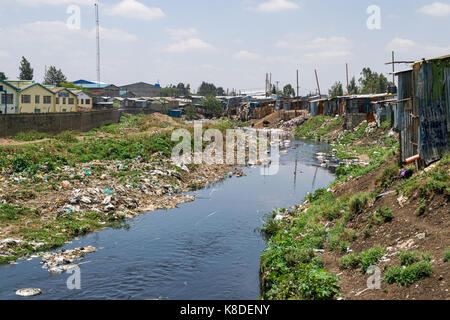 Baraccopoli baracche ed edifici linea il Ngong fiume che è inquinata con rifiuti, rifiuti in plastica e spazzatura, Nairobi, Kenia Foto Stock